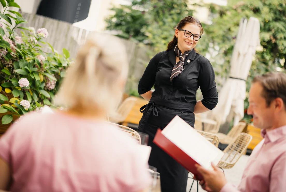 Kellnerin steht auf einer Terrasse und nimmt die Bestellung der Gäste auf
